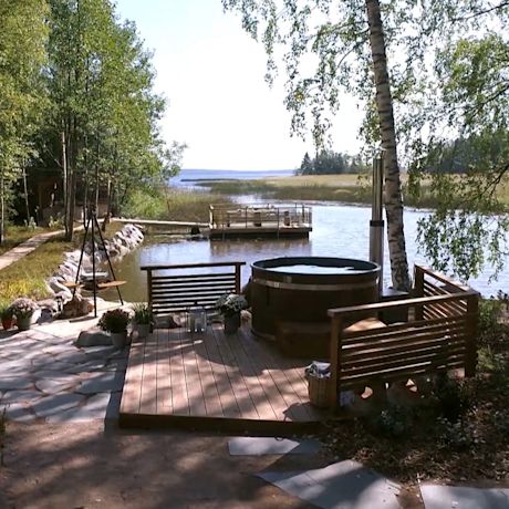 Puinen terassi ja kylpytynnyri järven rannalla koivujen varjossa.