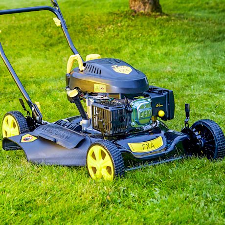 Musta-keltainen bensiiniruohonleikkuri vihreällä nurmikolla puun juurella