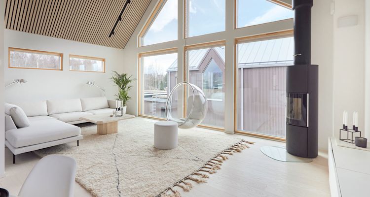 Vaalea olohuone isolla ikkunalla, valkoinen kulmasohva, roikkuva läpinäkyvä tuoli ja musta takka