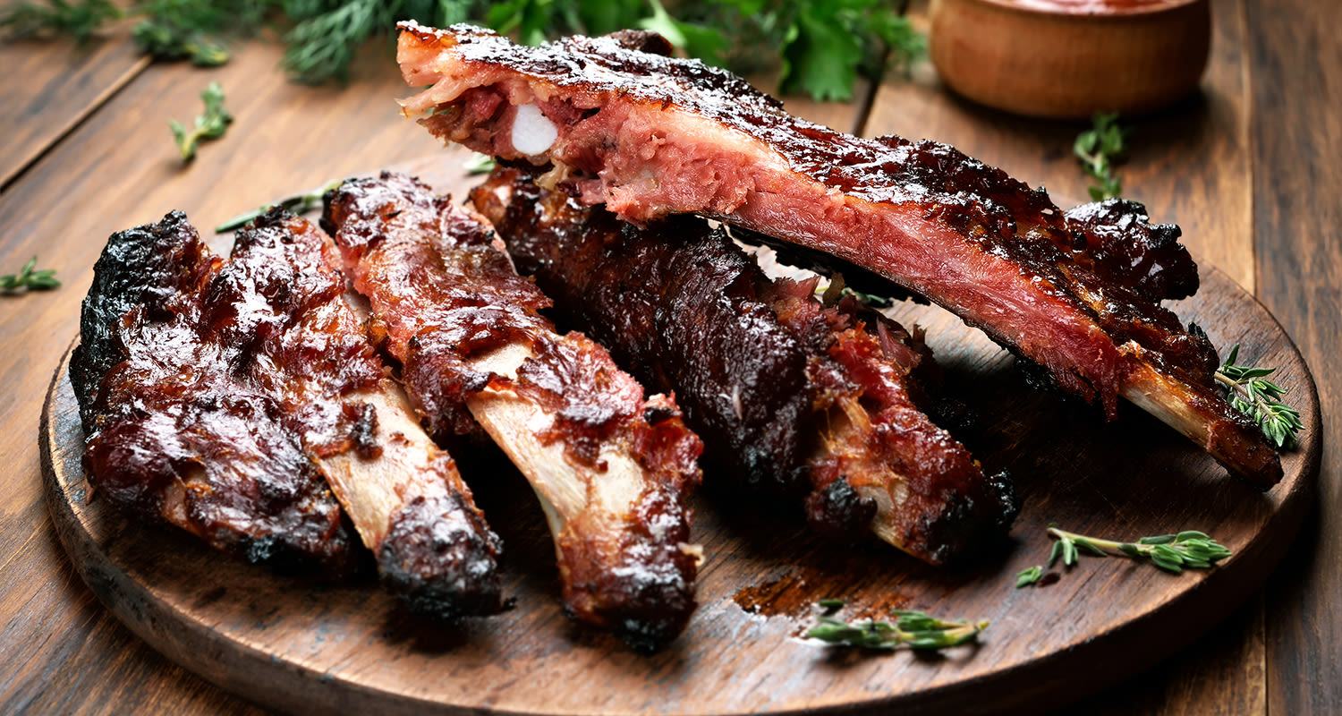 Savustettuja BBQ-kylkipaloja tumman laudan päällä rosmariinin oksien kera