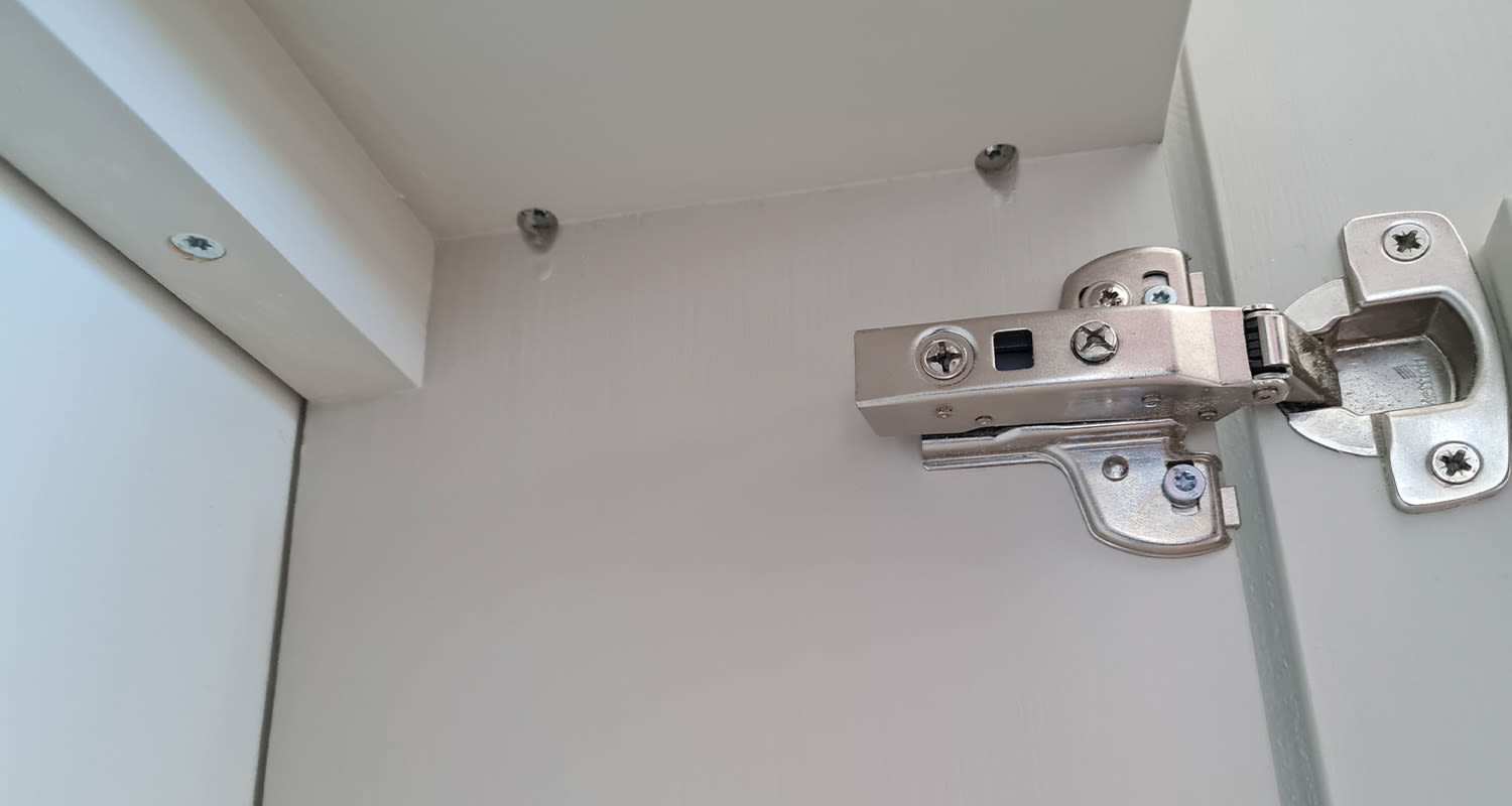 Avoimen valkoisen kaapin sisänurkka, oikeassa yläkulmassa hopeinen piilosarana.