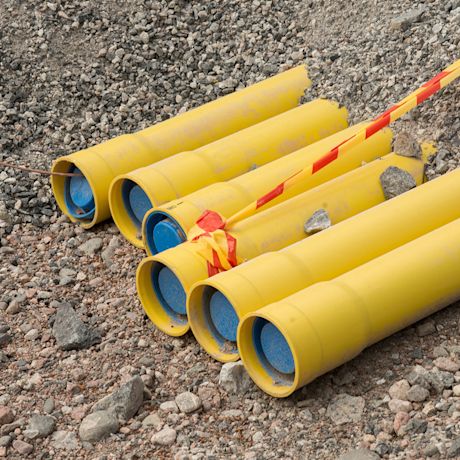 Pinottuja keltaisia muoviputkia ja punakeltainen varoitusnauha soralla.
