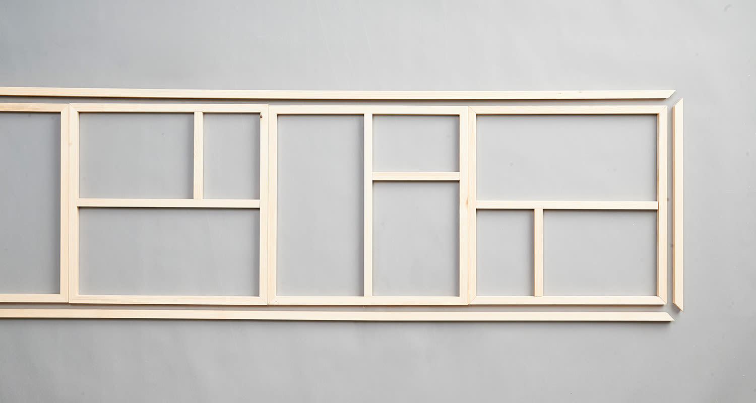 Vaalea puukehys jaettuna eri kokoisiin laatikoihin harmaata seinää vasten