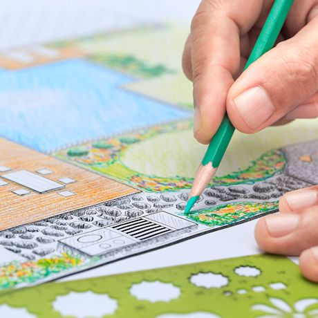 Käsi värittää vihreällä kynällä piha- ja puistosuunnitelmaa: sininen allas, nurmi, terassi.