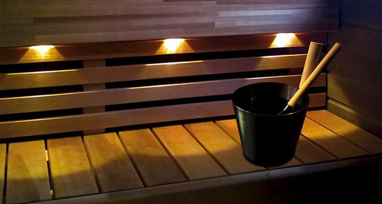 Saunan puisella penkillä musta vesisanko ja puinen kauha, keltainen tunnelmavalo.