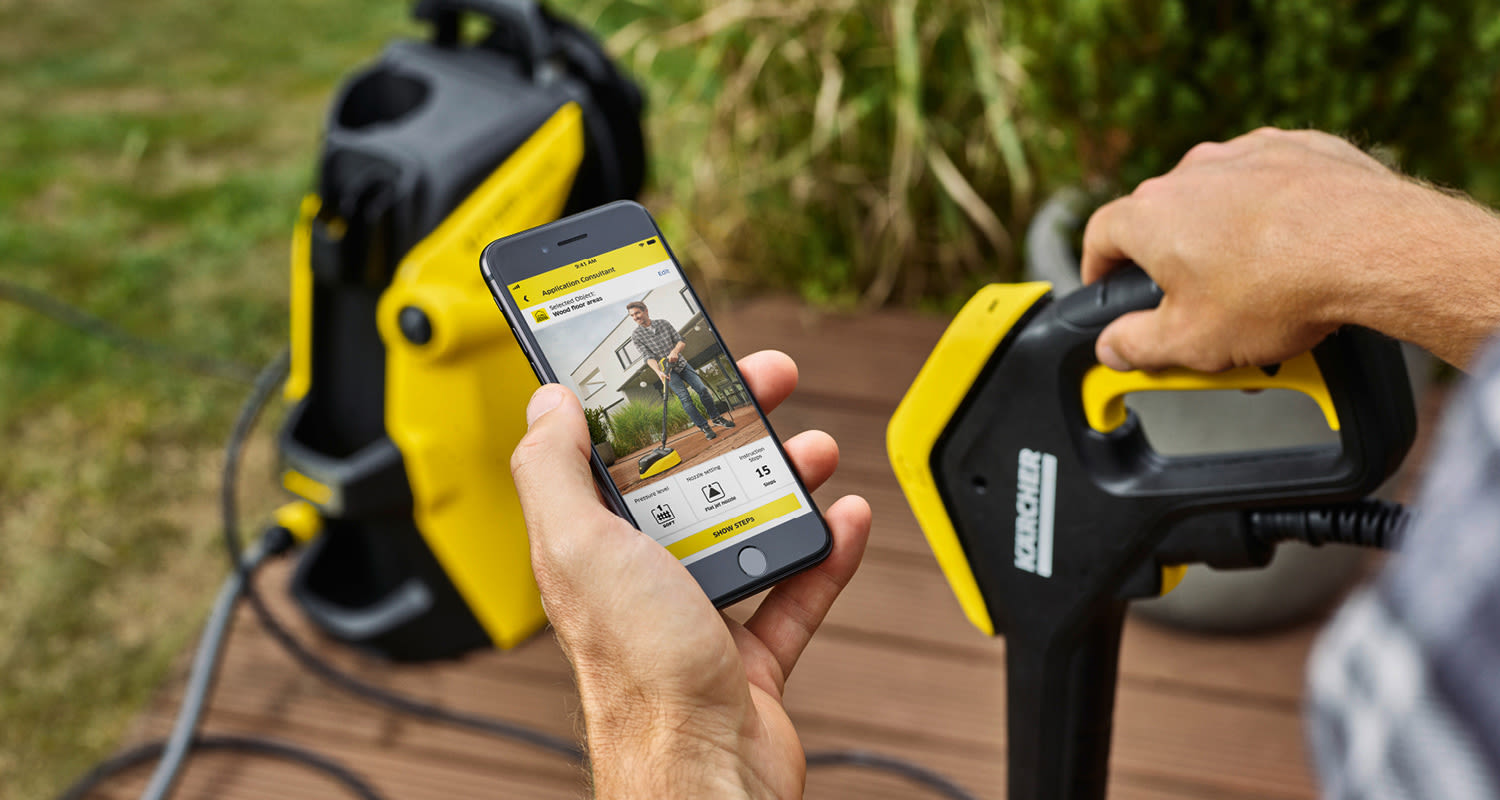 Keltamustaa Kärcher-painepesuria ja käsisuutinta, painepesurin ohjesovellus älypuhelimessa.