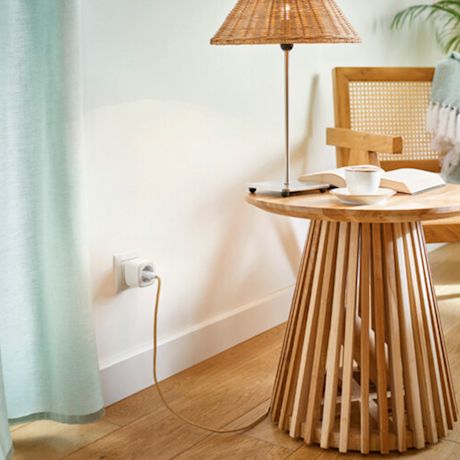 Lukunurkkaus: puinen sivupöytä rottinkilampulla, avoin kirja ja kahvikuppi vihreän verhon äärellä.