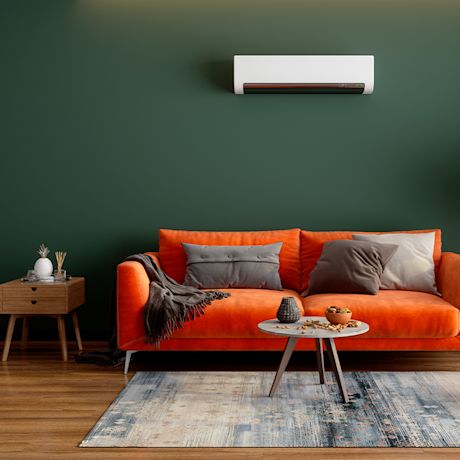 Oranssi sohva harmaine tyynyineen ja pieni pöytä, tumma vihreä seinä, valkoinen ilmastointilaite.