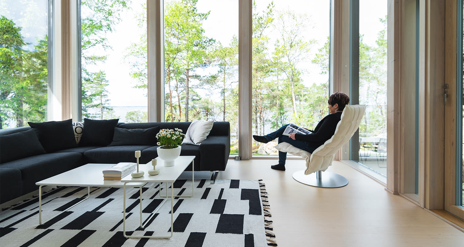Moderni olohuone: tumma kulmasohva, valkoinen pöytä, valkoinen nojatuoli ja metsänäkymä.