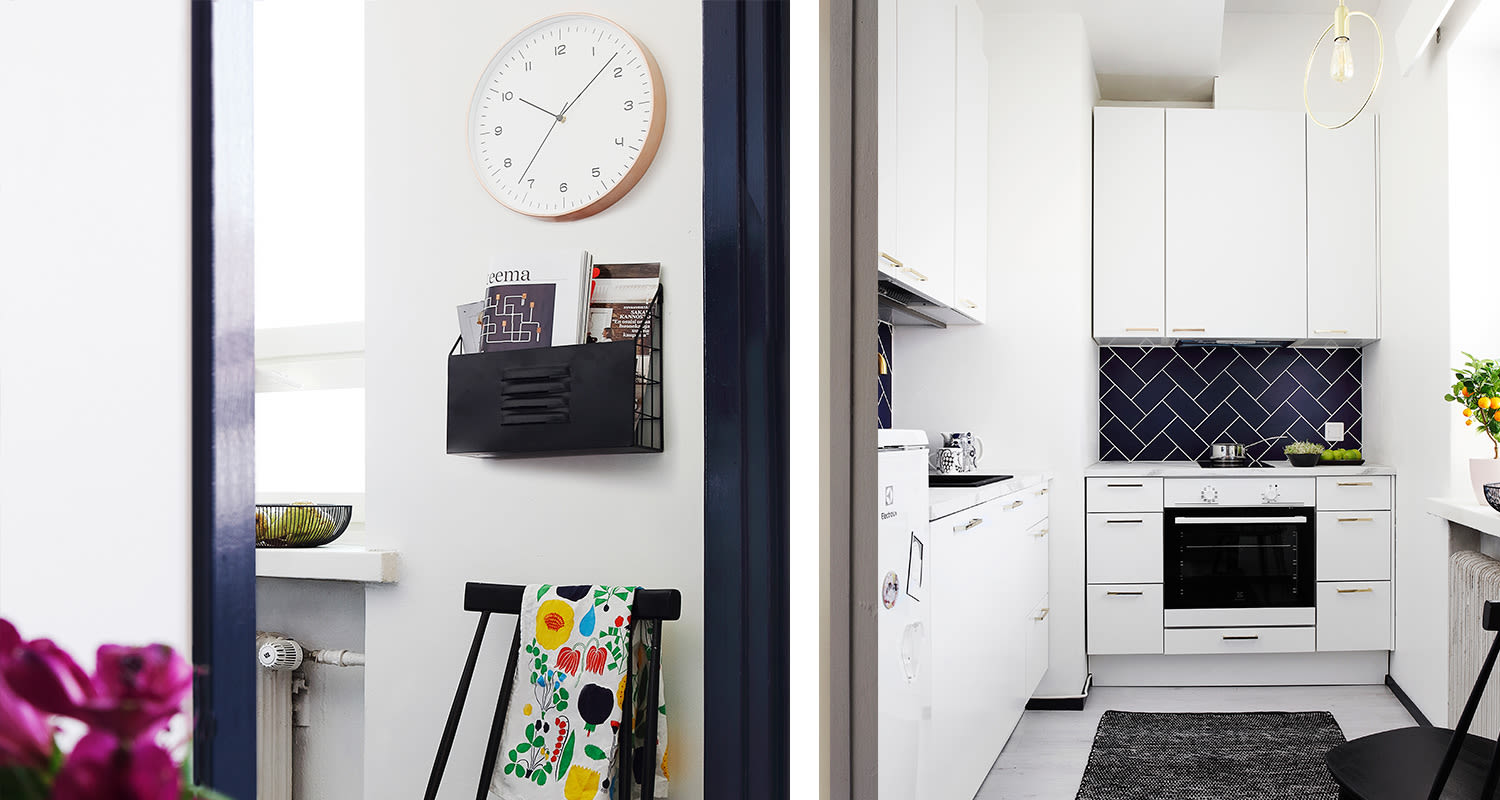 Valkoinen keittiö tummansinisin herringbone-laatoin, värikäs kukkapyyhe mustalla tuolilla