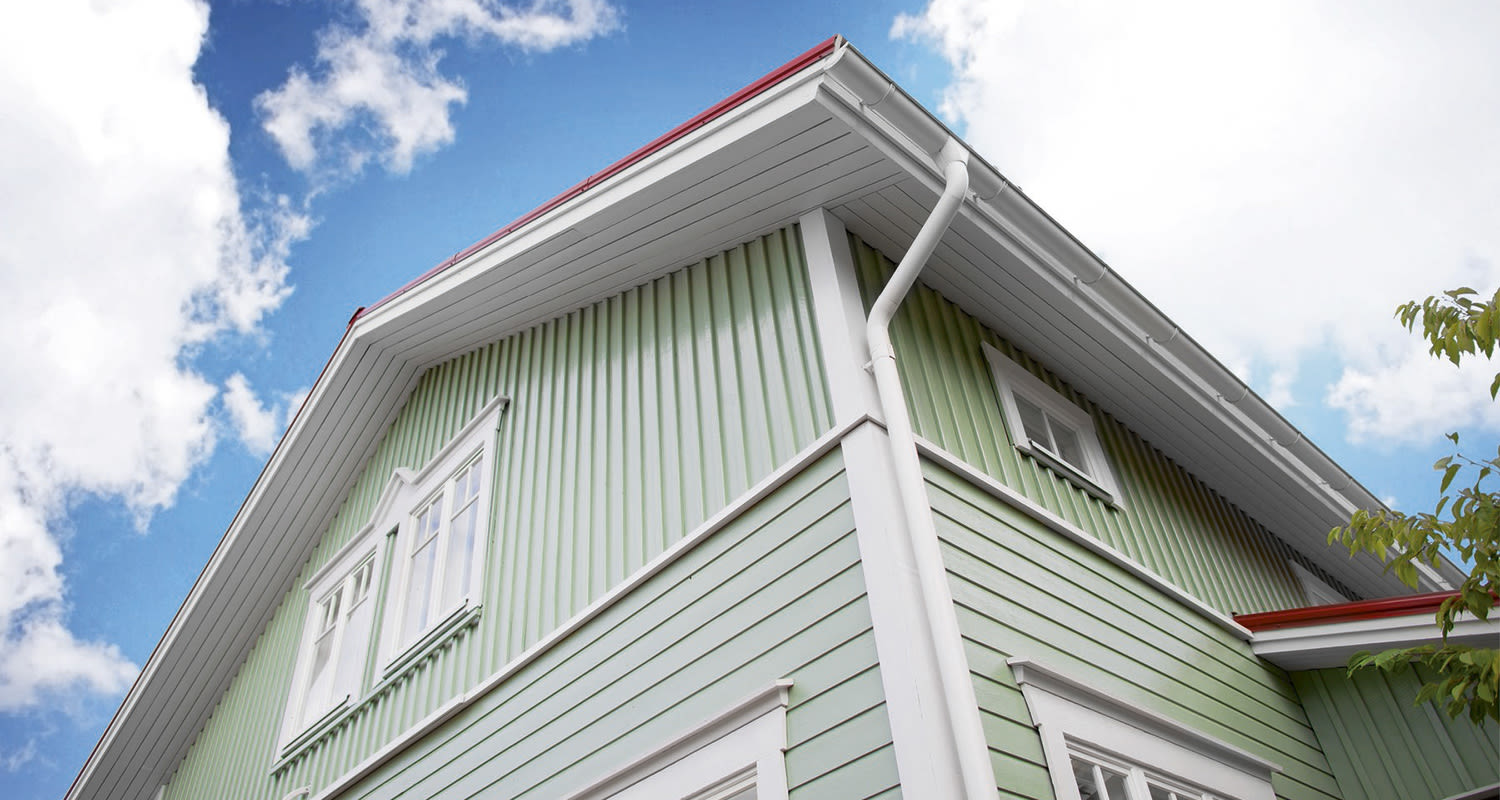 Vihreä puutalo valkoisin yksityiskohdin ikkunoilla, punareunaisella katolla sinistä taivasta vasten