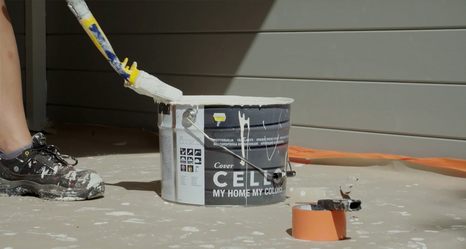 Valkoisella maalilla täytetty purkki ja tela maaliroiskeineen lattialla oranssin teipin vieressä