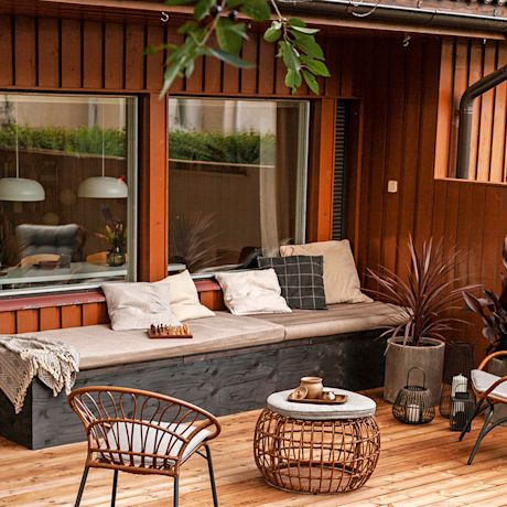 Ruskea terassi, penkillä harmaat tyynyt ja shakkilauta, rottinkituolit ja pikkupöytä teekannulla