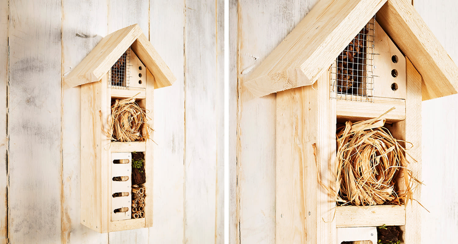 Vaalea puinen hyönteishotelli valkoisella seinällä: kolopesät, olkinippu, bambuputket.