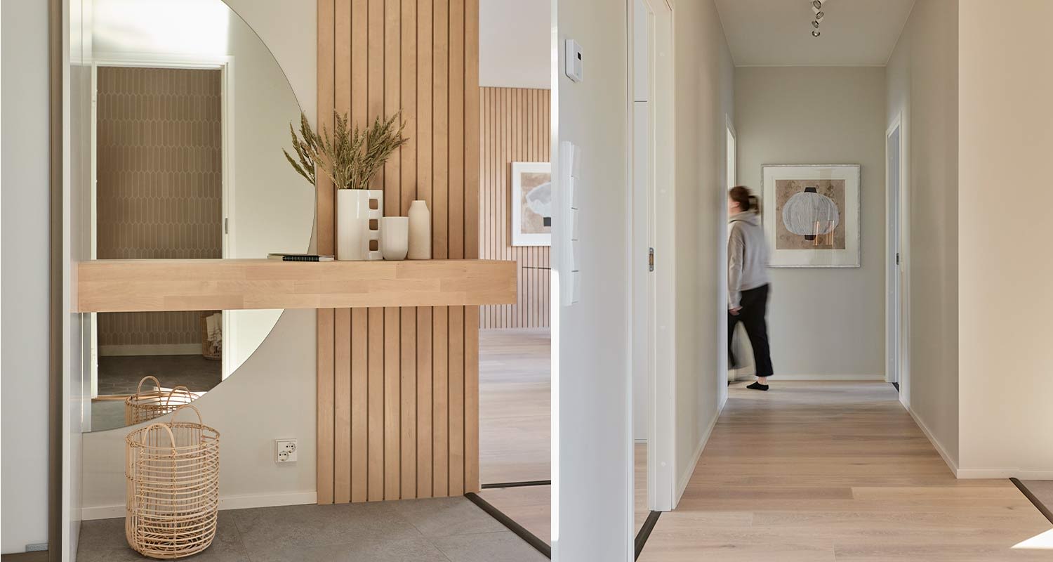 Vaalea eteiskäytävä, pyöreä peili, puupaneelit, hylly maljakoineen, rottinkikori ja kävelijä.