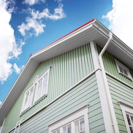 Vaaleanvihreä lautatalo valkoisilla listoilla, punaisella katolla ja sinisellä taivaalla