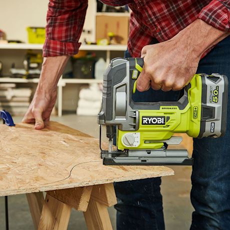 Mies punaruutuisessa paidassa leikkaa vihreällä Ryobi-pistosahalla lastulevyä työpajassa.