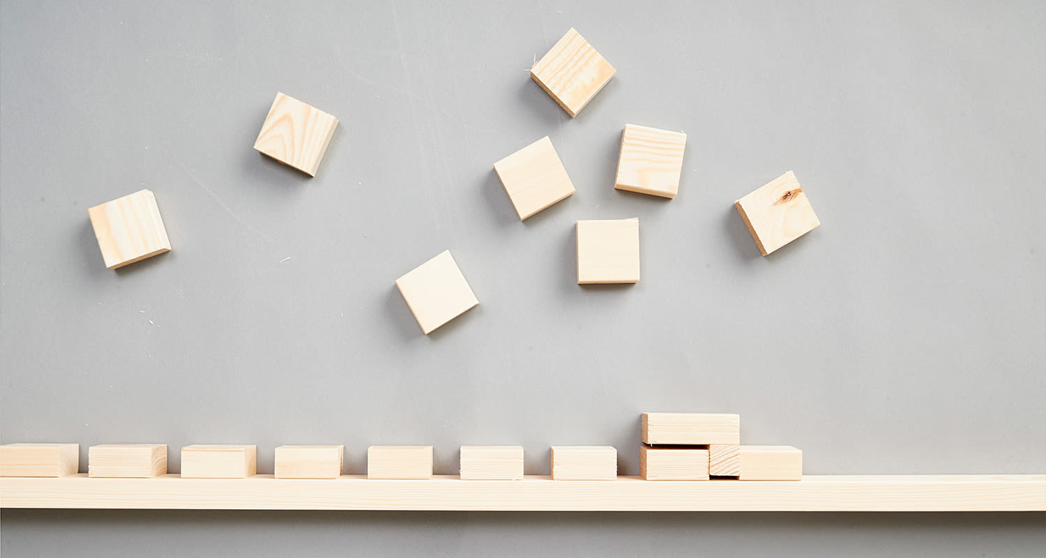 Harmaalla taustalla vaaleita puukuutioita, osa alarivin rivissä, osa hajallaan yläpuolella.