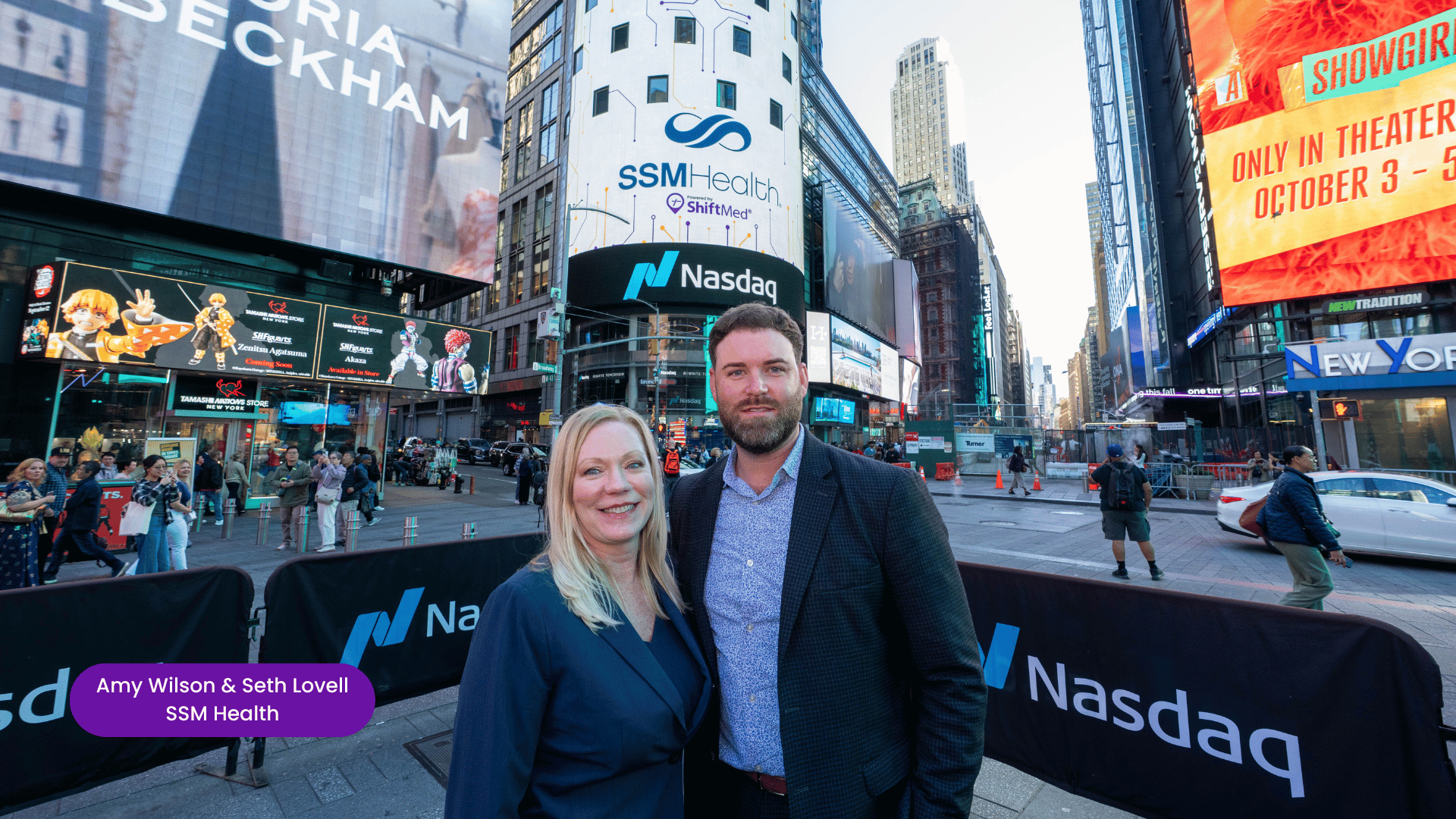 Amy Wilson, System Chief Nurse Executive at SSM Health, and Seth Lovell, System Vice President of Nursing Transformation and Innovation at SSM Health, stand in front of the Nasdaq screen in Times Square during the 2025 ShiftMed Workforce Innovation Summit.