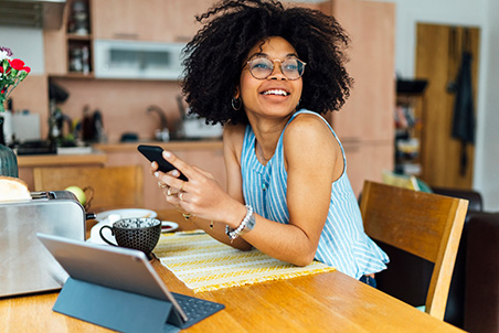 Woman-Smiling-in-Kitchen-w-Phone-and-Tablet-452x302