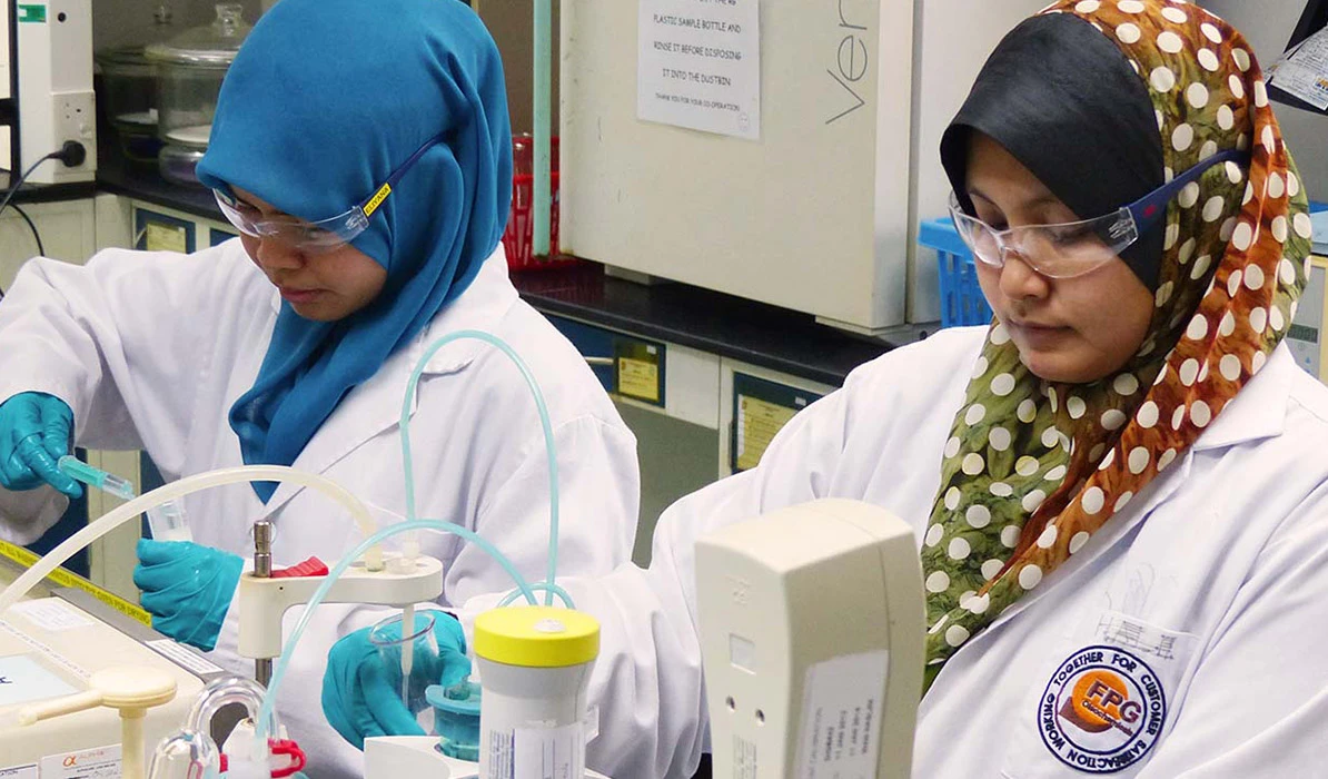 Two women in lab coats working with scientific equipment in a laboratory setting, focused on their tasks.