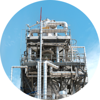 Industrial chemical processing plant with tall structures and storage tanks under a clear blue sky.