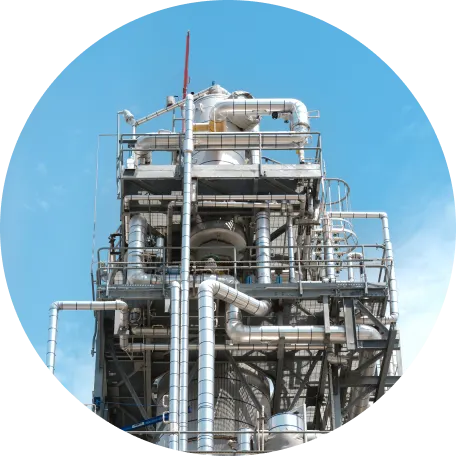 Industrial chemical processing plant with tall structures and storage tanks under a clear blue sky.