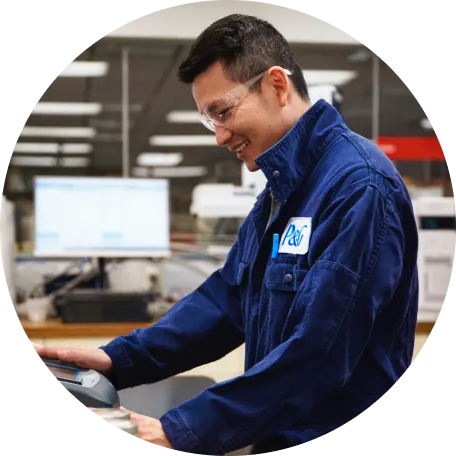 A man in a blue jacket, working on equipment with a focused expression in a well-lit facility.