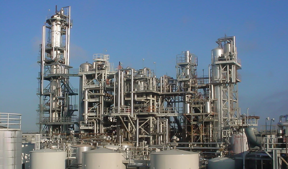Industrial chemical processing plant with tall structures and storage tanks under a clear blue sky.