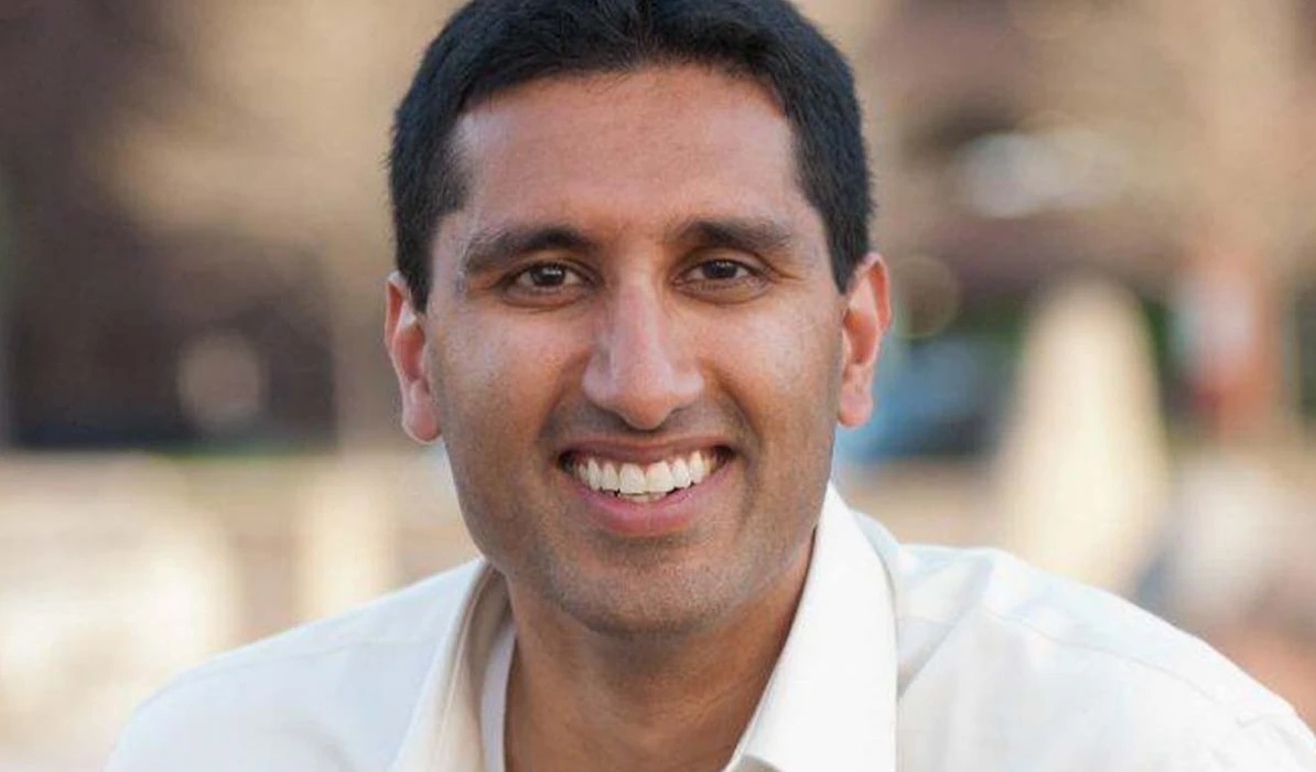 Smiling man wearing a white shirt, outdoors with a blurred background.