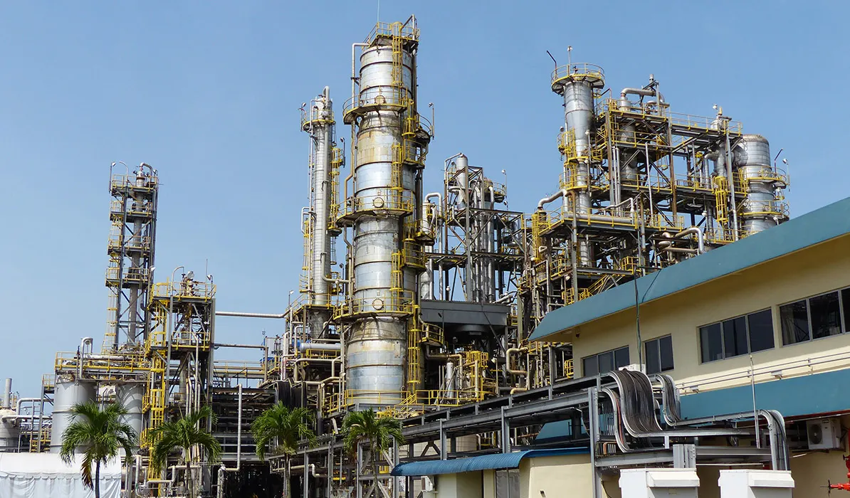 Industrial complex with numerous large pipes, towers, and tanks against a clear blue sky.