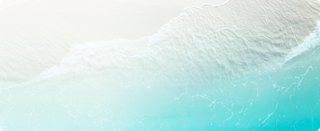 Aerial view of a sandy beach with gentle waves lapping at the shore, featuring clear turquoise water and white sand.