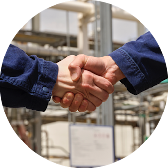 Handshake between two individuals wearing work attire in an industrial setting.