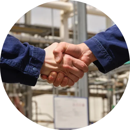 Handshake between two individuals wearing work attire in an industrial setting.