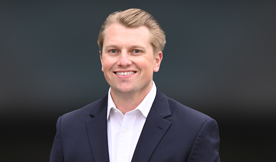 A young man in a suit, looking forward with a smile on his face.