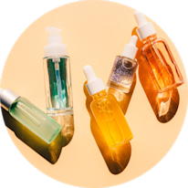 Assorted skincare oils in glass dropper bottles arranged on a circular surface, showcasing different colors and textures.