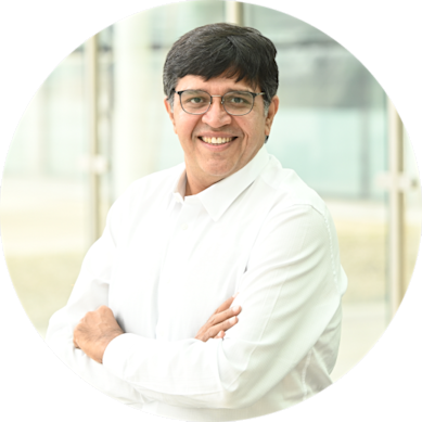 Smiling man wearing glasses and a white shirt, posing with arms crossed in front of a bright, modern background.