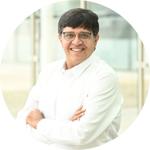 Smiling man wearing glasses and a white shirt, posing with arms crossed in front of a bright, modern background.