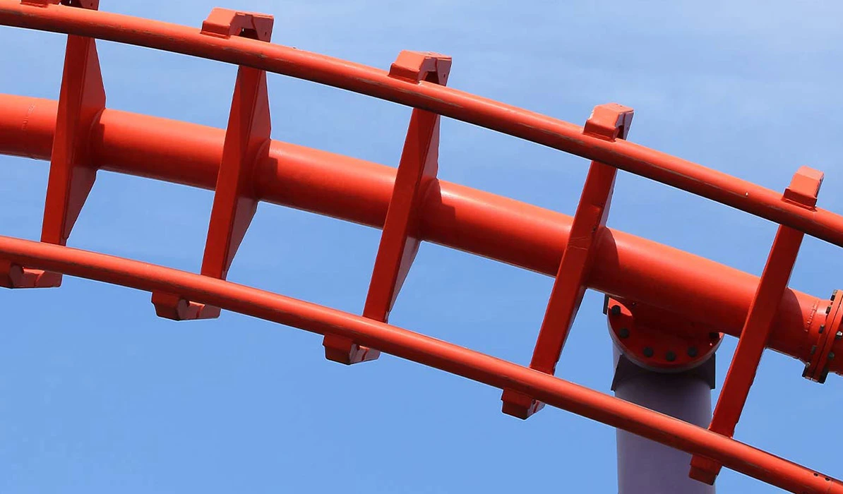 Close-up of a red roller coaster track against a clear blue sky.