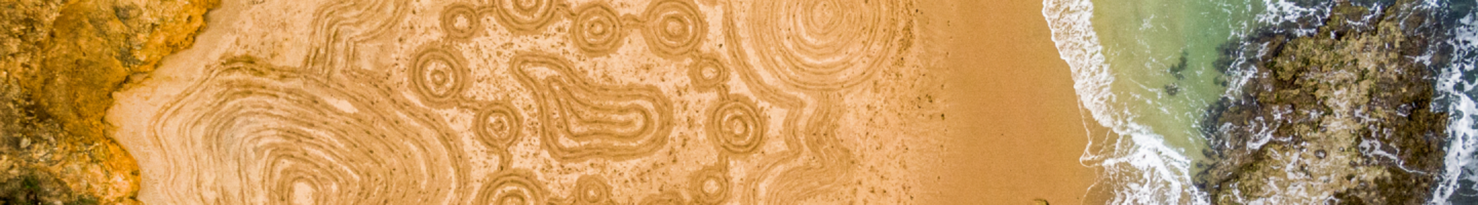 A huge traditional Indigenous drawing in sand taken on a beach from above during the day.