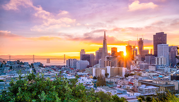 Skyline van San Francisco bij zonsondergang, met wolkenkrabbers, de Golden Gate Bridge en de zee. 