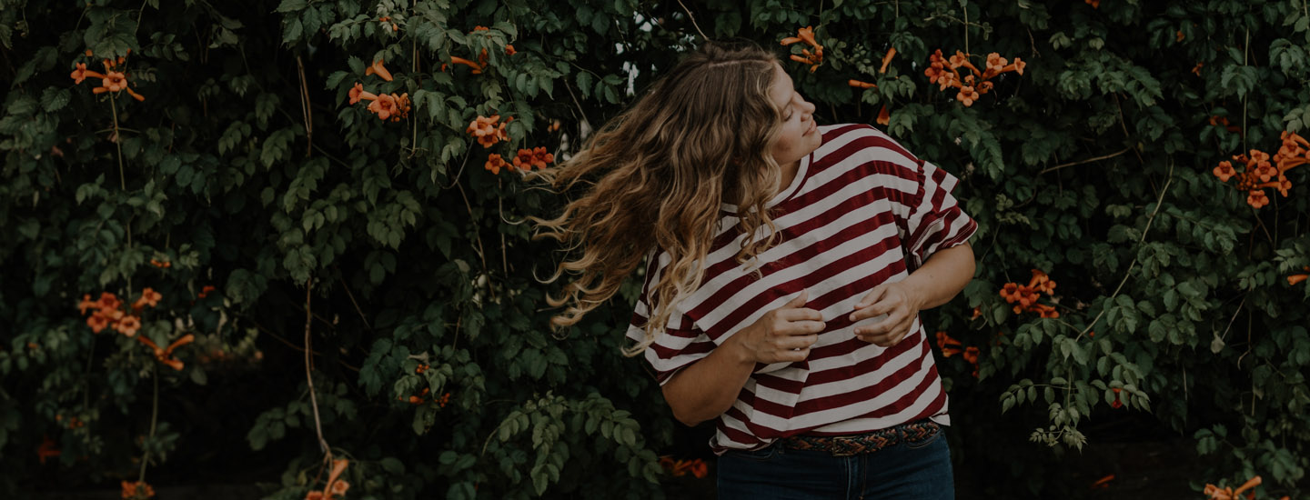 Woman standing in front of flowers flipping her hair in the wind.