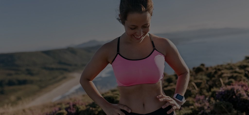 Smiling woman resting after a run on cliffs next to the ocean.