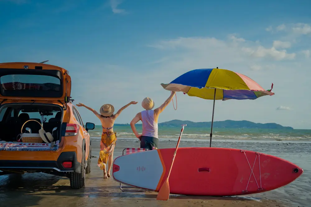 Viaggi - Vacanze estive dark Viaggi vacanza al mare, ragazzi sulla spiaggia con ombrellone, tavola da surf e auto