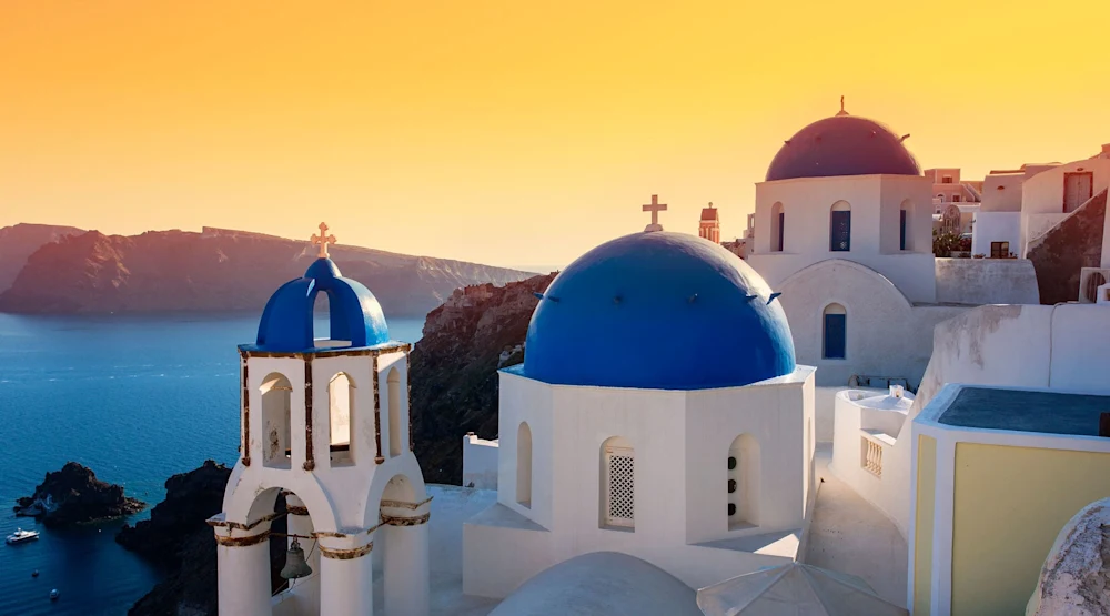 Assicurazione viaggio Grecia Tipiche case bianche con cupole blu affacciate sul mar Egeo al tramonto, icona delle isole greche e delle vacanze in Grecia in estate.