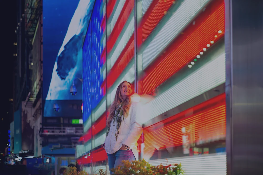 Hero Image / USA -Stati Uniti - New York Ragazza che sorride a New York di sera con sfondo uno schermo luminoso che proietta la bandiera americana