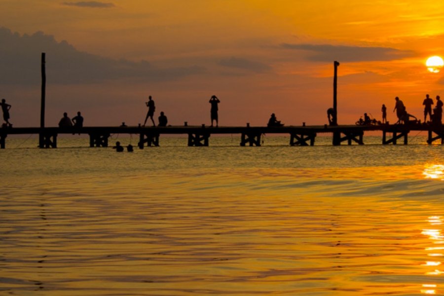 Un atardecer en Holbox con siluetas de turistas y locales sobre el muelle empapados en la brillante luz naranja