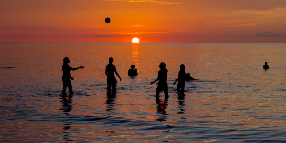 Touristas en Holbox jugando en el mar con un balón y el atardecer atraz de ellos