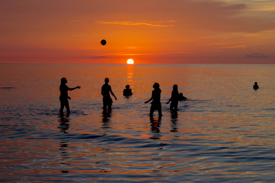 Holbox Island visitors playing with a ball in the sea with the sunset behind them