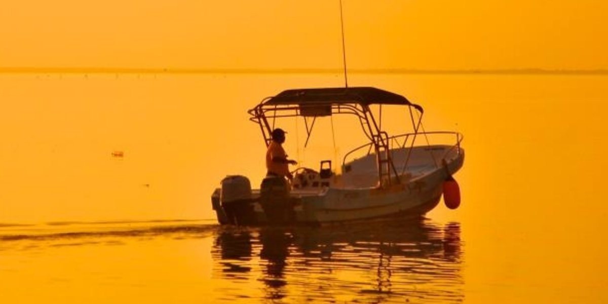 Amanecer en Holbox sobre la laguna Conil, un pescador en su lancha sale a trabajar
